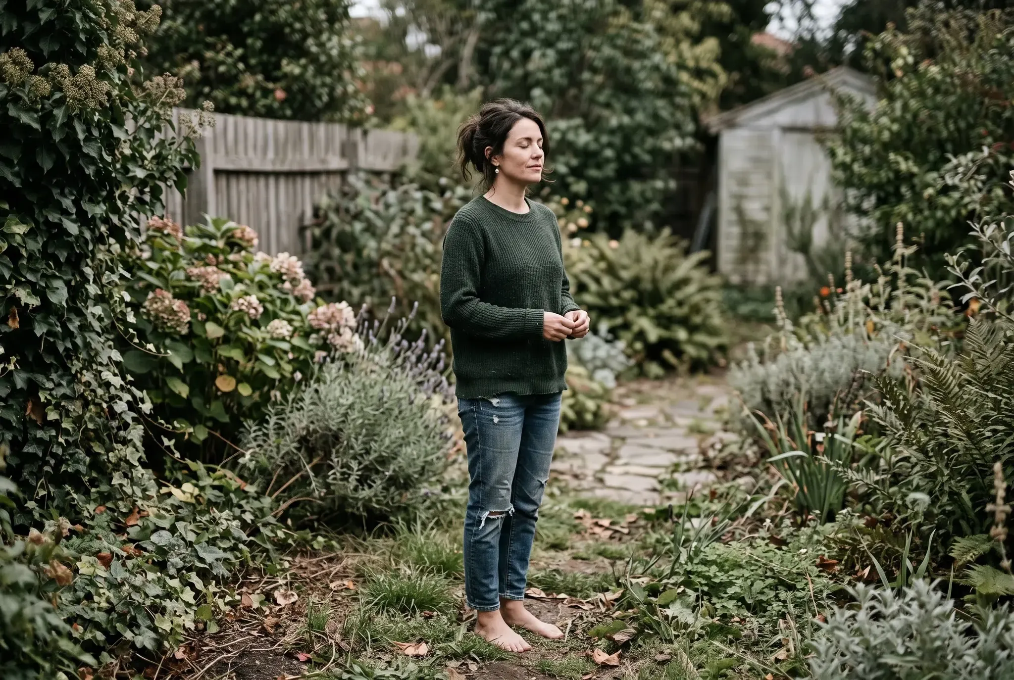 A woman standing barefoot on grass in a garden, weight settled through her feet