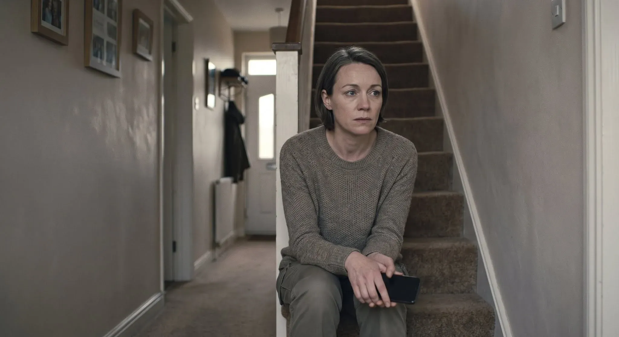 A woman sitting on the stairs at home with her phone in her hands, staring ahead as she tries to work out what just happened