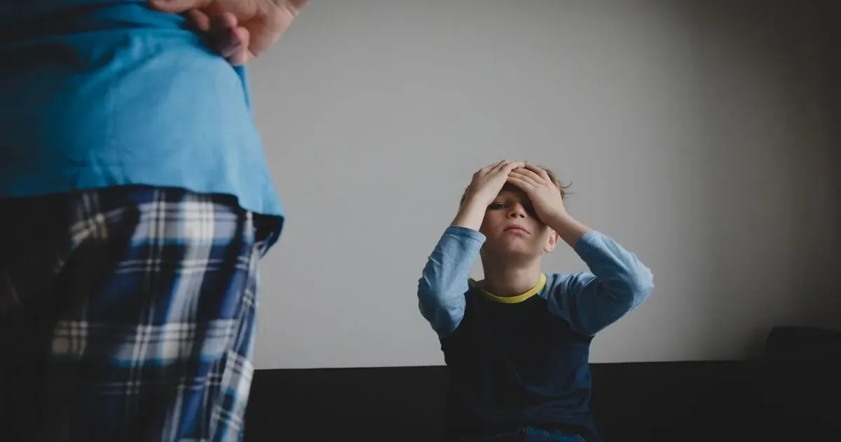 A woman standing over a young child who is holding their head in their hands