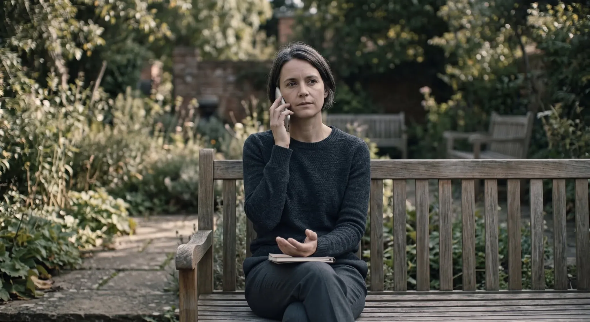 A woman on a garden bench on a phone call, calm and composed, one hand resting open in her lap